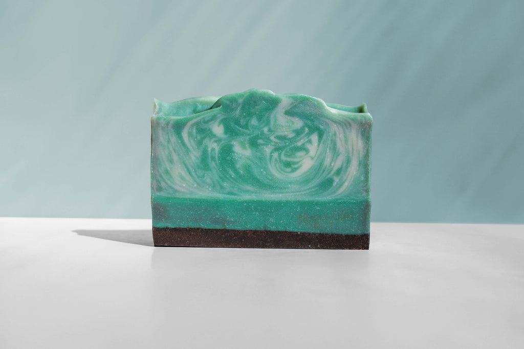 Green and white swirled soap bar on a white surface with a light gray background