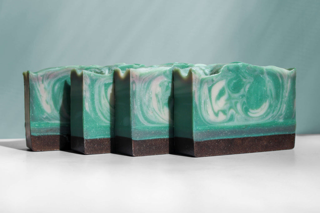 Four bars of green and brown soap with a marbled pattern on a white surface.