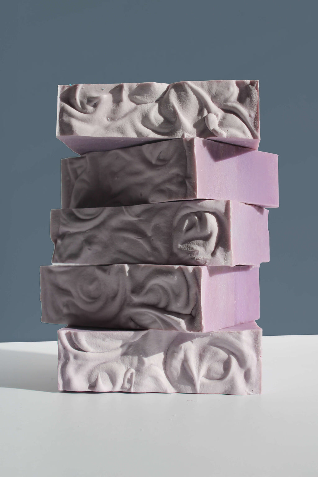 Stack of purple and gray soap bars on a light gray surface with a dark gray background