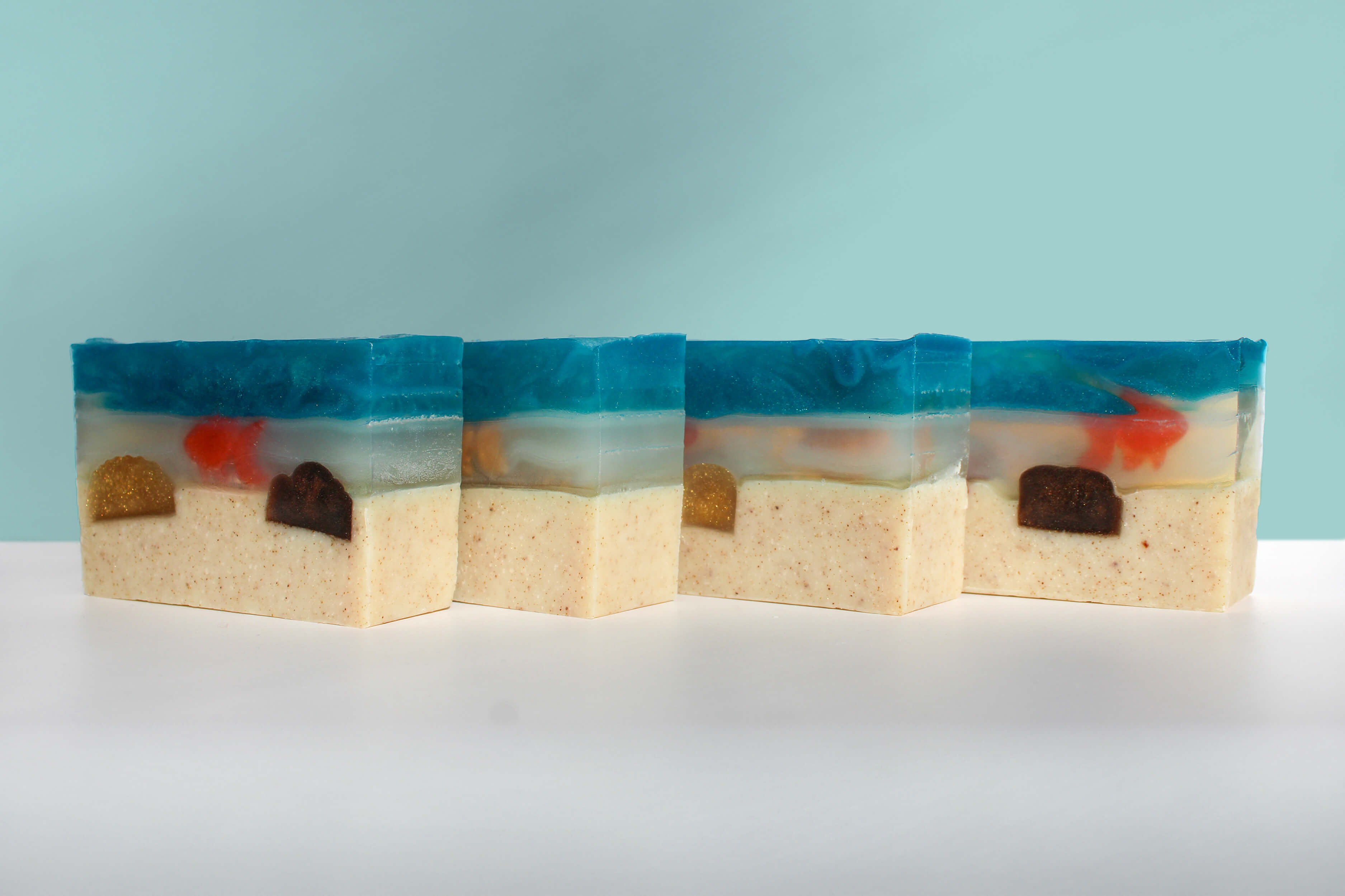 Four rectangular soap bars with beach-themed designs on a white surface and light blue background