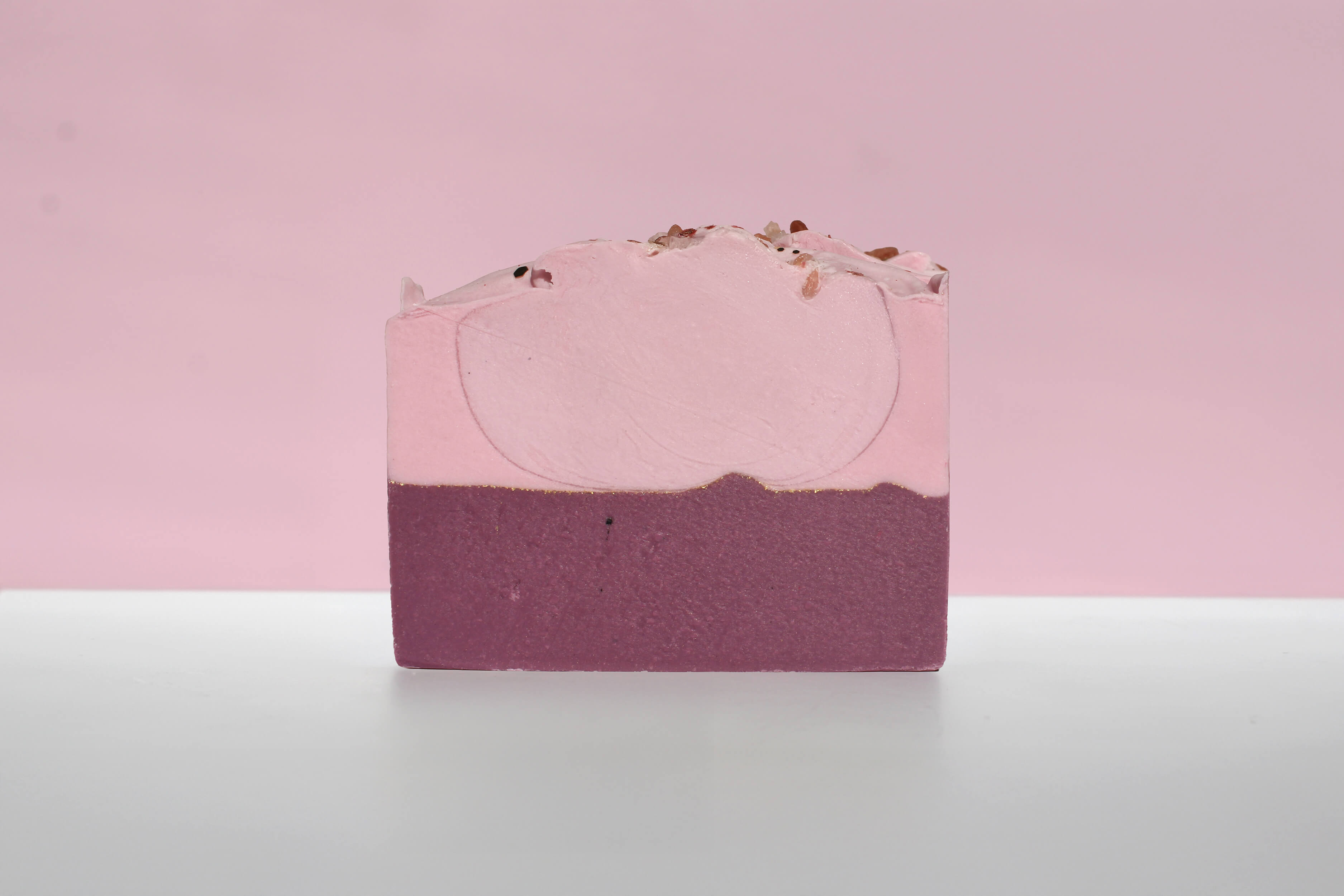 Bar of soap with pink and purple gradient on a light pink background