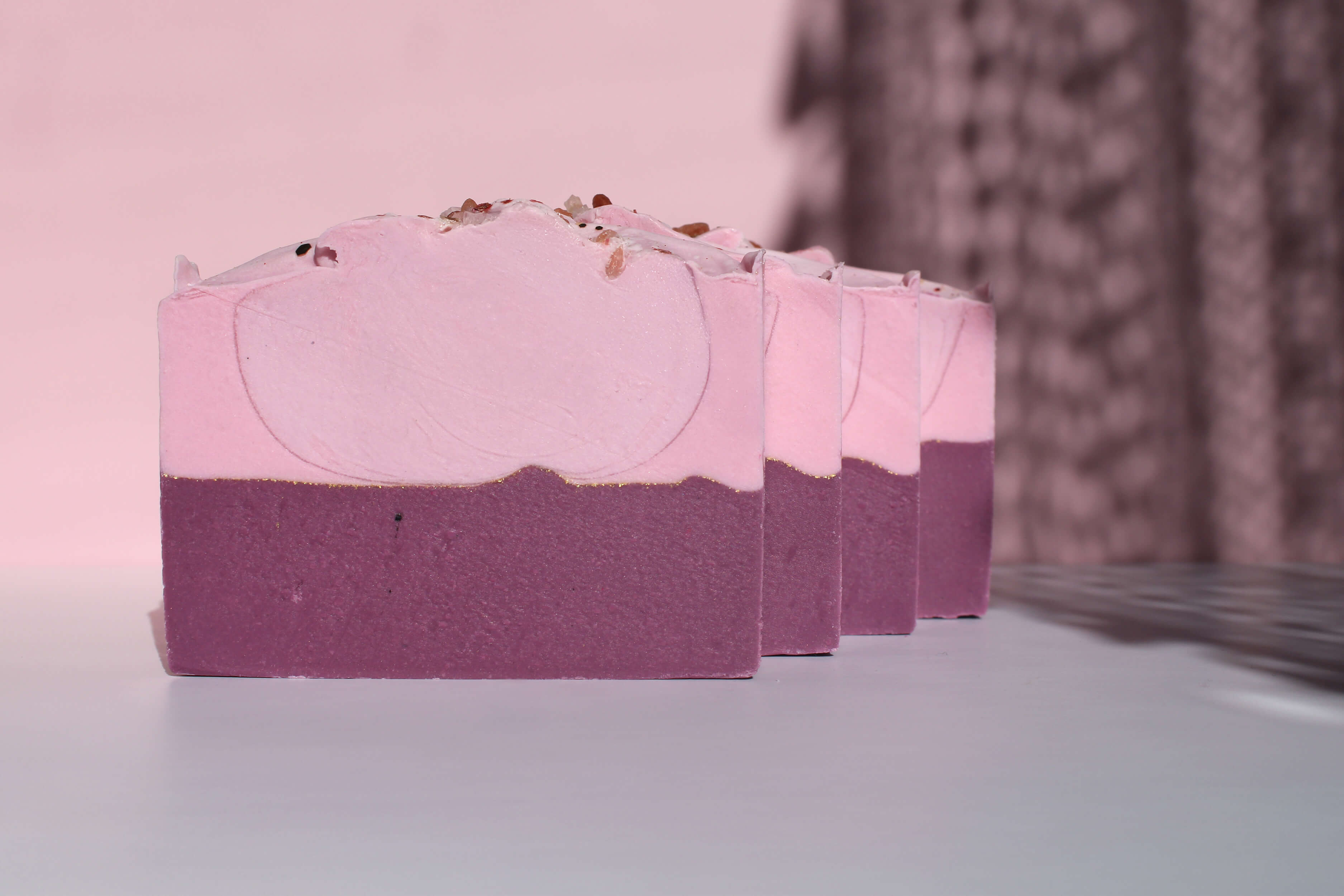 Three pink and purple soap bars on a light surface with a blurred background
