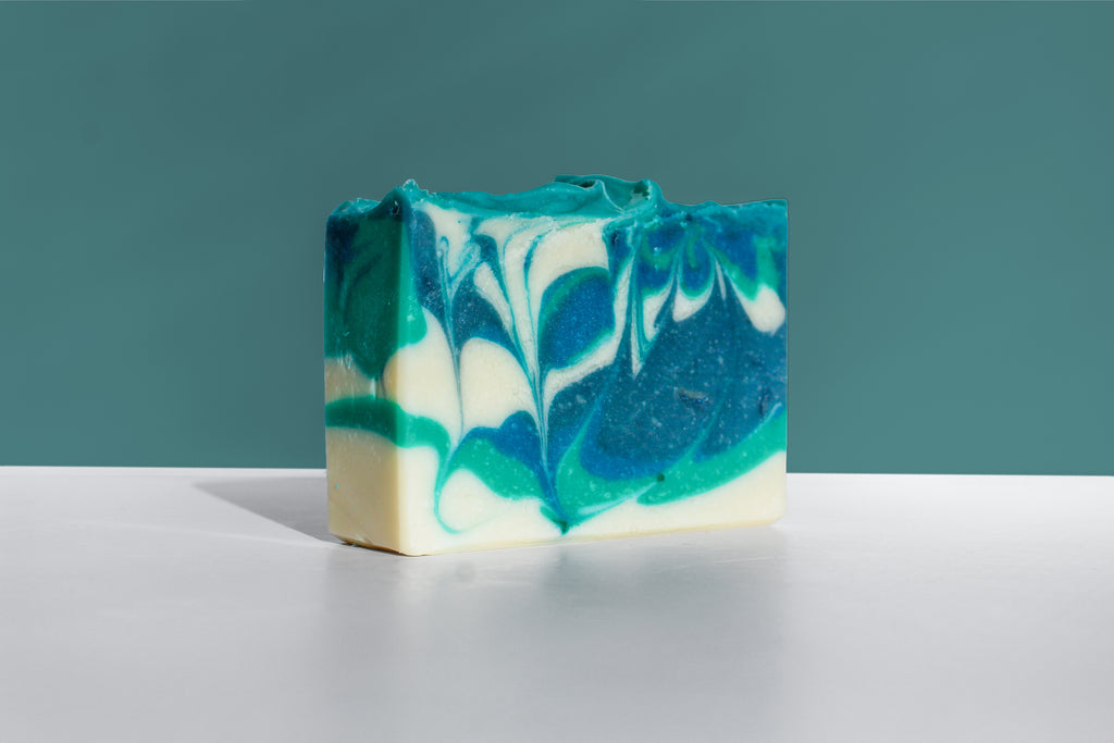 Bar of soap with blue and green swirls on a gray surface and teal background