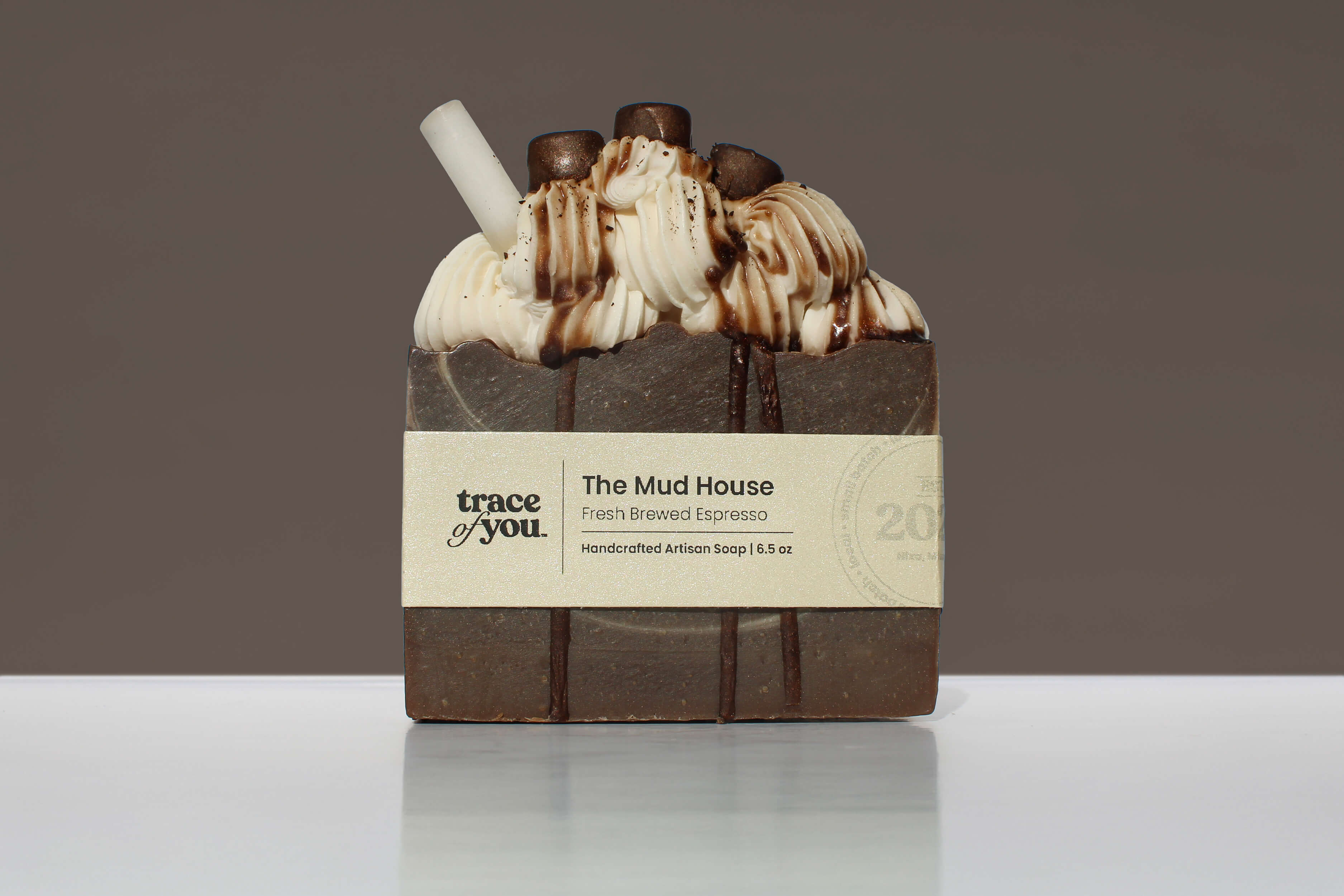 Bar of soap with chocolate drizzle and 'The Mud House' branding on a gray background