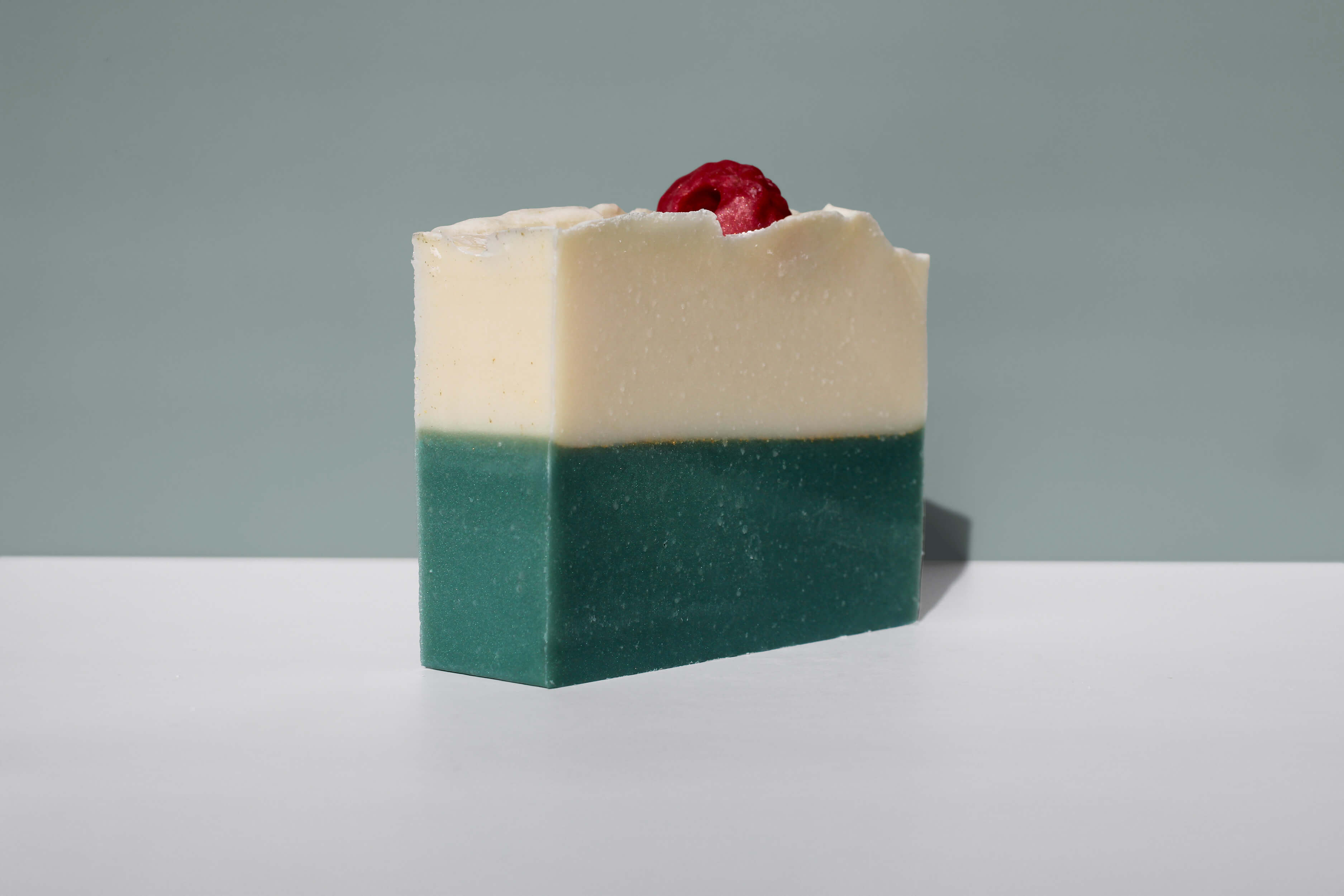 A bar of soap with a raspberry on top, on a gray background.